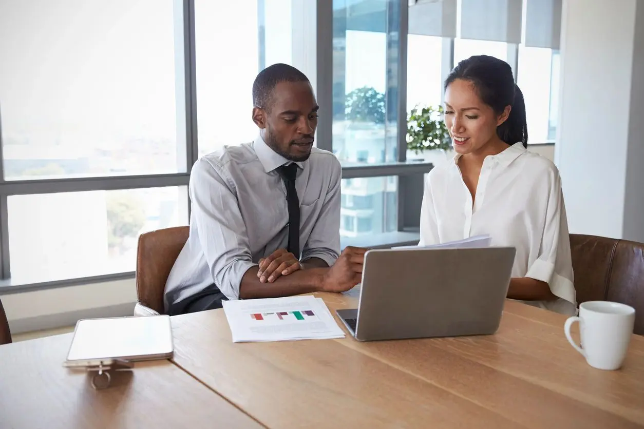 Two professionals discussing work at desk.