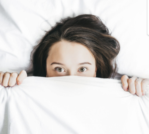 A woman hiding under the covers in bed