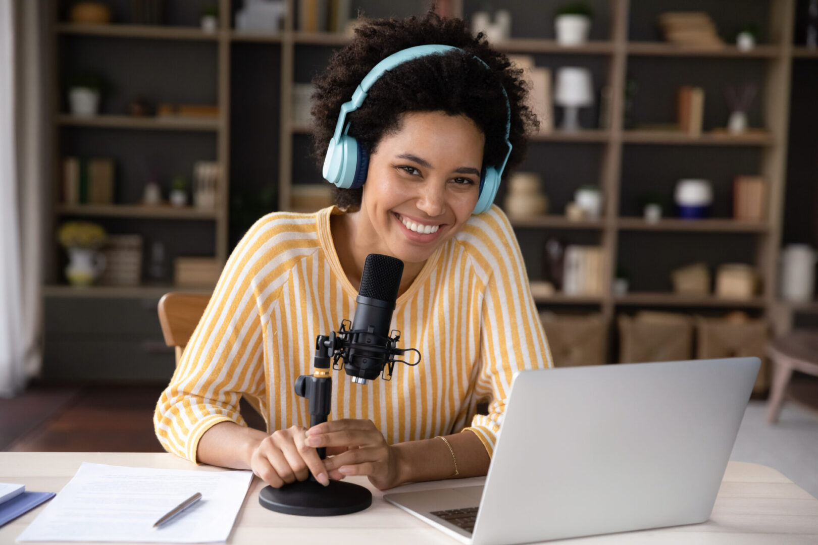 Happy young Black woman in headphones and professional microphone recording Woman podcasting with microphone and laptop.