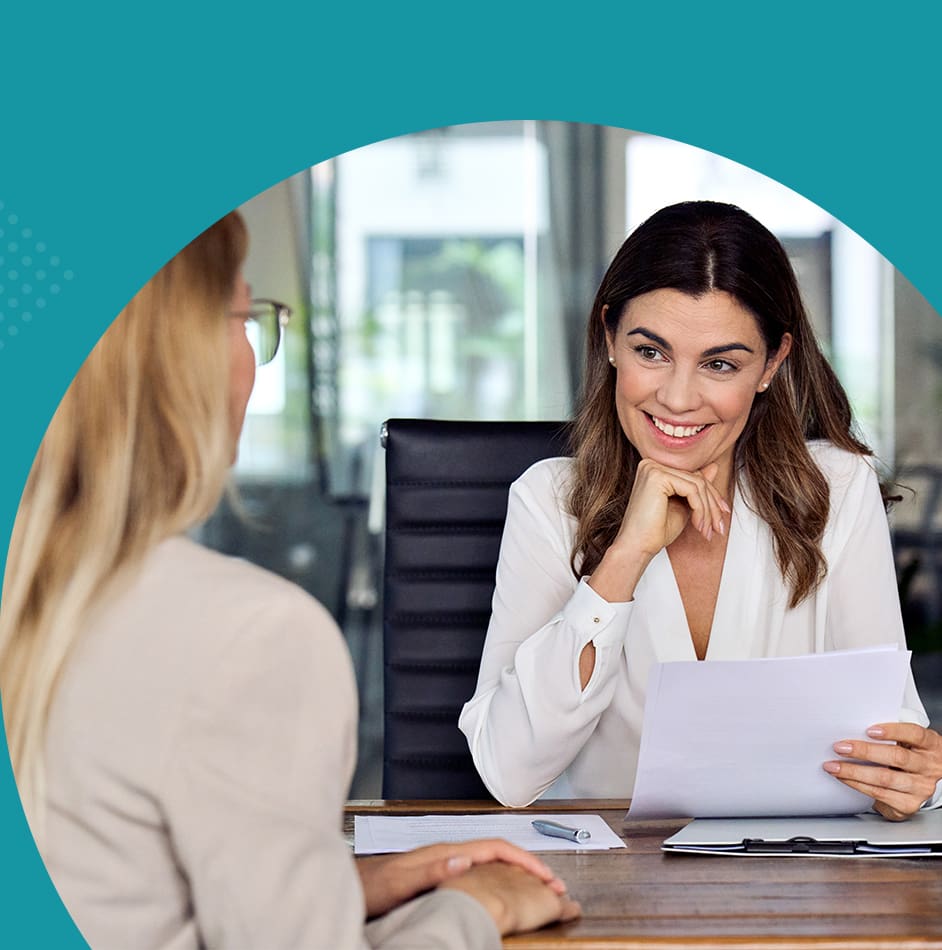 Two women discussing documents in a modern office setting.
